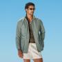 Mid green field jacket with raglan shoulders and a sleek hip-length cut. Features hidden snap buttons, zip closure, and an interior waist drawstring. Includes flapped and slanted pockets.